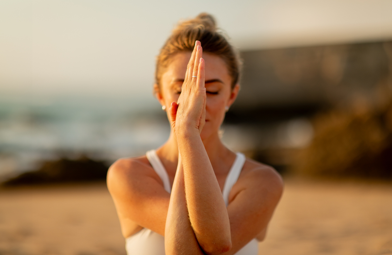 Woman Performing hands-together meditation on beach